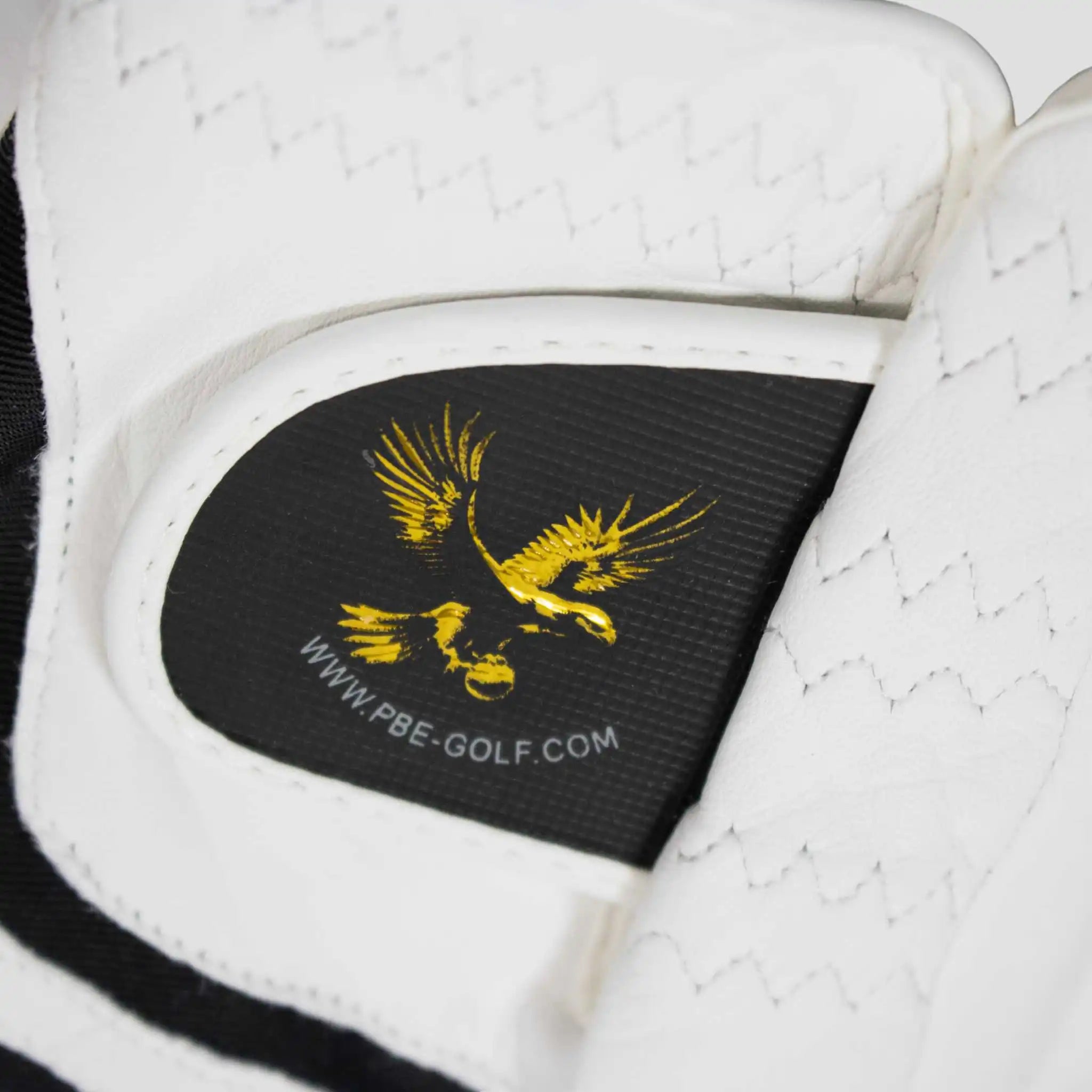 White golf glove with a black patch featuring a gold eagle logo and 'PBE-GOLF.COM' text.