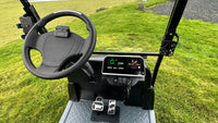 Steering wheel and dashboard of a golf cart on a grassy field
